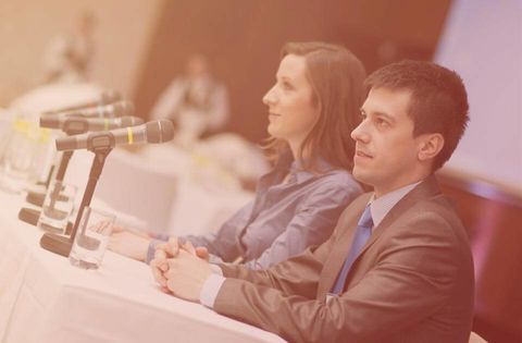 Zwei Personen am Tisch mit Mikrofonen während einer Konferenz