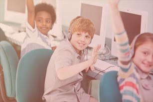 drei sich meldende Kinder vor Pcs, mit Kopfhörern