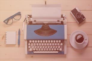 Schreibmaschine auf einem Tisch von oben, darum verteilt eine Tasse Kaffee, ein Notizblock, eine Brille und eine Kamera