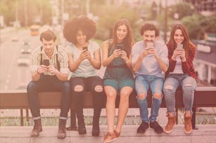 Eine Gruppe Studenten sitzt nebeneinander auf einer Bank, jeder von ihnen blickt auf sein Smartphone