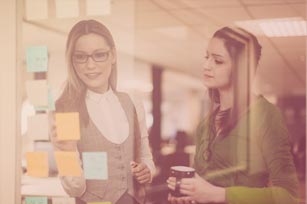 Medienmanagerinnen betrachten Klebezettel auf einer Glaswand