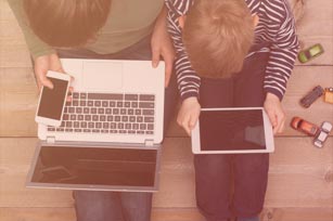 Zwei Jungen sitzen mit Laptop, Tablet und Smartphone auf dem Boden eines Kinderzimmers